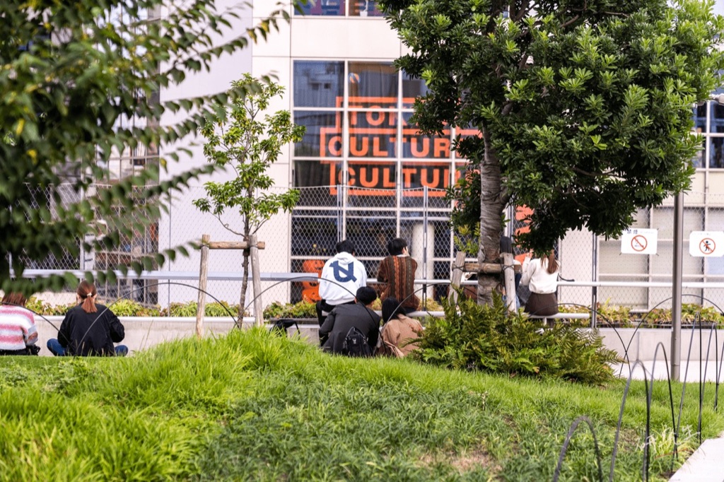 大草皮上坐著休息的人,遠處是寫著 CULTURE 的橘色牆面